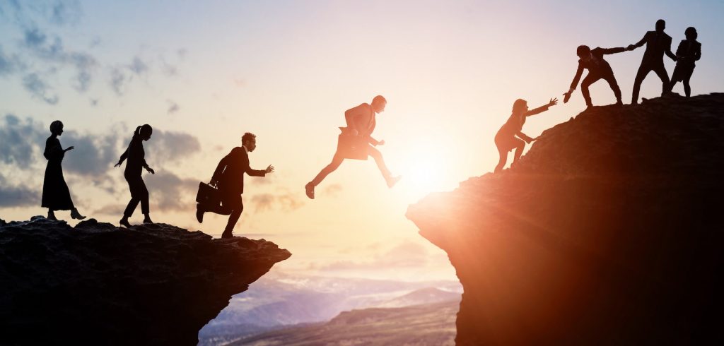 people wearing business suits and helping one another leap across a chasm