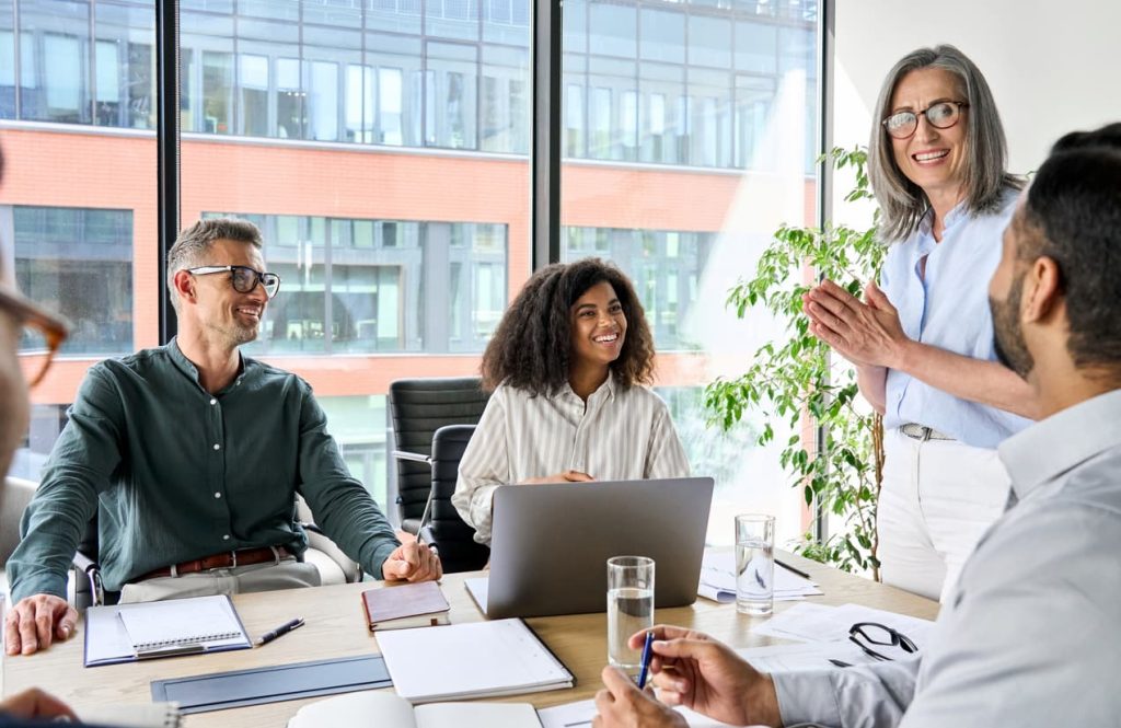 mature woman standing and addressing a group of people in an office meeting